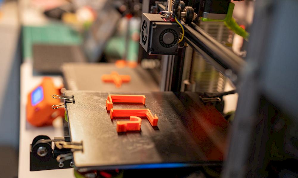 Frisch gedruckte orangefarbene Kunststoffhalterungen auf dem Druckbett eines 3D-Druckers