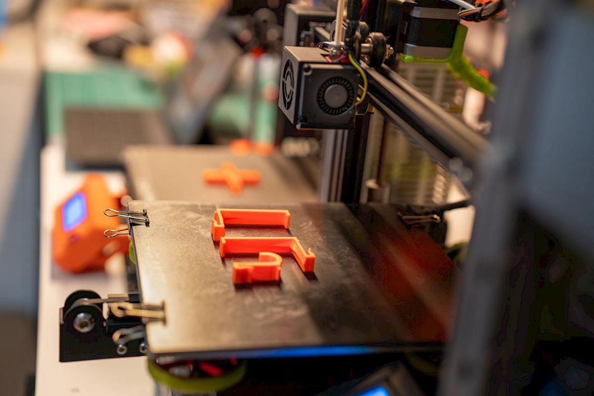 Frisch gedruckte orangefarbene Kunststoffhalterungen auf dem Druckbett eines 3D-Druckers